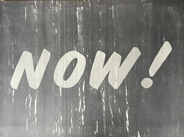 The word NOW with an exclamation mark painted in pale letters on a dark ground.